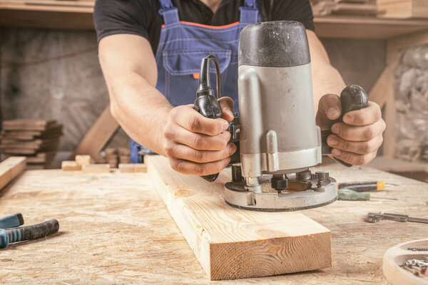 Young man by profession carpenter builder equals a wooden milling machine on a wooden table in the workshop