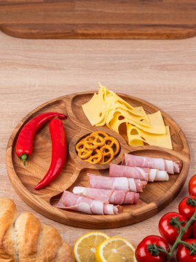 Tahta tepside çeşitli peynirler, sosisler ve sebzeler. Peynir tabağı, bayram sofrası için atıştırmalıklar..