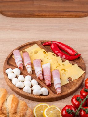 Yuvarlak ahşap tabağın üst görüntüsü farklı aperatifler: sosisler, peynir, biberler, ahşap bir masanın üzerinde duran.