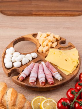 Yuvarlak ahşap tabağın üst görüntüsü farklı aperatifler: sosisler, peynir, biberler, ahşap bir masanın üzerinde duran.