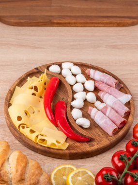 Tahta tepside çeşitli peynirler, sosisler ve sebzeler. Peynir tabağı, bayram sofrası için atıştırmalıklar..