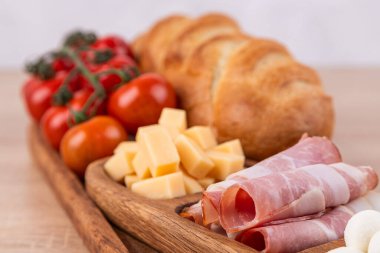 Tahta tepside çeşitli peynirler, sosisler ve sebzeler. Peynir tabağı, bayram sofrası için atıştırmalıklar..