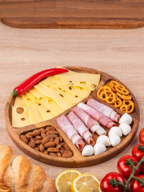 Pişmiş etler, peynir ve sebzeler, ahşap bir tahtada domates ve ekmekle servis edilir.