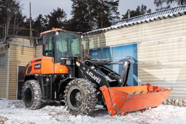 Novosibirsk, Rusya - 29 Şubat 2024: Turuncu traktör, garaja karşı yükleyici