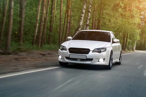 stock image A white  new  sedan  is driving along a highway in the forest