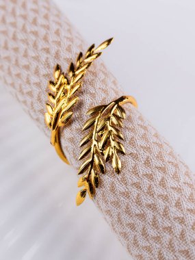 Kumaş peçeteli tabaklar, masasında yapraklar ve çatal bıçaklarla dekoratif altın yüzük.