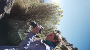 Telefonuyla dağlarda bitkileri fotoğraflayan bir adam.