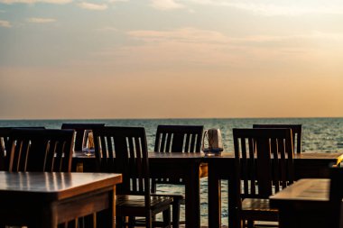 Antika ahşap masalar ve Tayland sahilindeki bir restoranın sandalyeleri. Günbatımı saati, deniz ve gökyüzünün bulanık arkaplanı. Metin ve tasarım için boş alan.