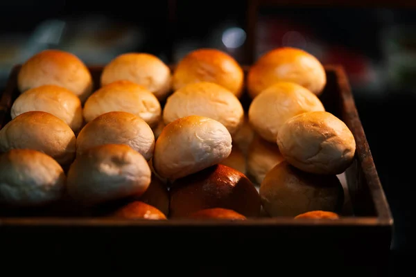 Hot Fresh Baked Bread Rolls in a wooden box for the customer, the stack of fresh baked bread rolls, warm light from above, dark food image, front view.