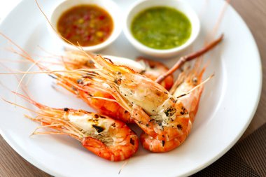 İki farklı soslu ızgara karides, yeşil soslu deniz ürünleri ve tatlı kırmızı biber sosu. Tabakta ızgara karides. Pencereden doğal ışık geliyor. Yemek görüntüsünü kapat..