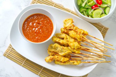 Moo Satay, Tayland usulü, fıstık soslu ve salatalı domuz şişi. Tahta şişleri olan bambu bir hasırın üzerinde beyaz bir tabakta servis edilen Tayland yemeği..