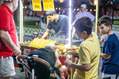 İstanbul, Türkiye - 14 Temmuz 2022: Geleneksel Türk arabasında müşterilere hizmet veren erkek sokak fast food satıcısı. Gece sahnesi.