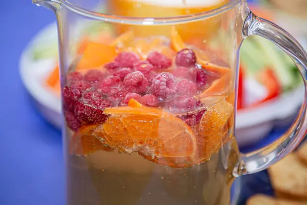 Decanter of chilled refreshing fruit drink with pieces of orange and berries. Close-up.