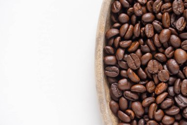 Kahve çekirdekleri ve beyaz üzerine ahşap tabak. Kahverengi kahve çekirdeklerinin üst görüntüsü. Kapat..