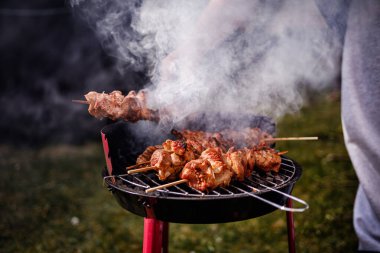 Kömür ızgarasında pişen sulu salamura edilmiş et şişleri. Birisi onlara maşa kullanırken duman yükseliyor..