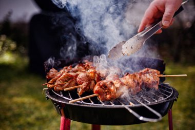 Kömür ızgarasında pişen sulu salamura edilmiş et şişleri. Birisi onlara maşa kullanırken duman yükseliyor..