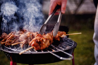 Kömür ızgarasında pişen sulu salamura edilmiş et şişleri. Birisi onlara maşa kullanırken duman yükseliyor..