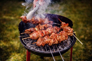 Kömür ızgarasında pişen sulu salamura edilmiş et şişleri. Birisi onlara maşa kullanırken duman yükseliyor..
