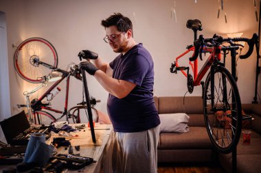 Eldivenli bir adam ev atölyesinde bisiklet tekerleğini inceliyor. Etrafı aletlerle, ışıklarla ve yaratıcı iç mekanlarda birden fazla bisikletle çevrili..