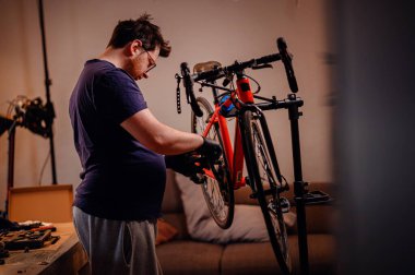 Eldiven giymiş odaklı bir adam, kapalı bir çalışma alanındaki tamir standına monte edilmiş kırmızı bir bisikletin krank setini ayarlar..