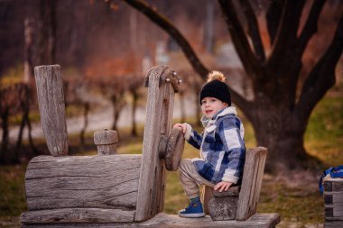 Rahat kışlık giysiler içindeki küçük çocuk parktaki ahşap bir trende mutlu bir şekilde oynuyor..