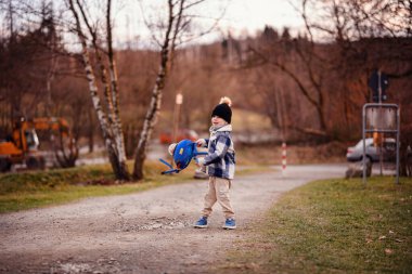 Rahat kışlık giysiler içindeki küçük çocuk dışarıda oyuncak ayıyla mavi bir roket çantası sallıyor..