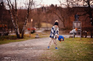 Rahat kışlık giysiler içindeki küçük çocuk dışarıda oyuncak ayıyla mavi bir roket çantası sallıyor..