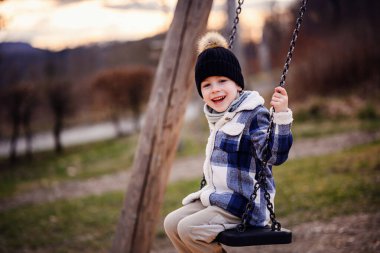 Kışın giydiği neşeli çocuk gün batımına yakın parkta salıncakta otururken ışıl ışıl gülümsüyor..