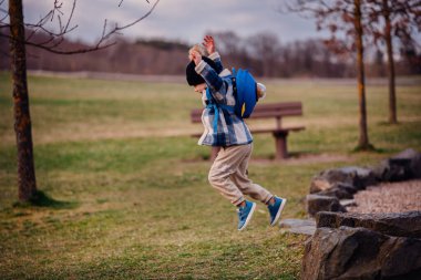 Kış kıyafetleri içinde enerjik bir çocuk parktaki kayaların arasına atlıyor. Üzerinde mavi bir roket çantası var..