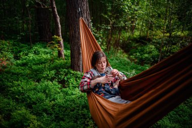 Bir anne, uyuyan oğlunu yemyeşil ormanlarla çevrili turuncu bir hamakta tutar. Birlikte sakin ve hassas bir anın tadını çıkarır..