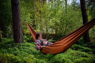Bir anne, uyuyan oğlunu yemyeşil ormanlarla çevrili turuncu bir hamakta tutar. Birlikte sakin ve hassas bir anın tadını çıkarır..