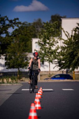 Genç bir insan güneşli bir günde kask ve giysi giyerek açık hava antrenmanında bisiklet sürüyor..