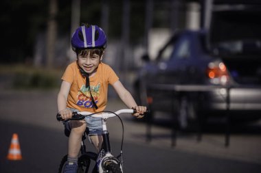 Kask takan genç bir çocuk, bir sıra trafik konisi boyunca küçük bir bisiklet sürüyor, güneşli bir yolda açık hava antrenmanı sırasında odaklanmış ve kararlı..