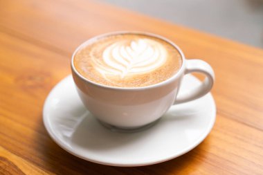 Ahşap masa arkasında beyaz bir fincanda sıcak Latte Kahve.