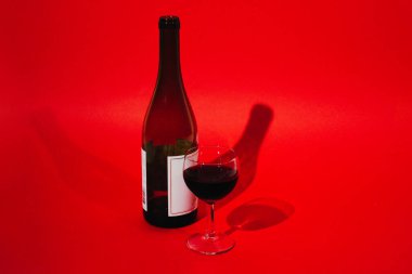 Kırmızı arka planda bir kadeh şarap olan kırmızı şarap şişesi.