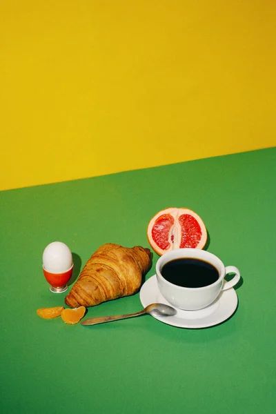 breakfast with croissant, coffee, and fruits on yellow background