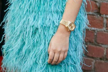 MILAN, ITALY - SEPTEMBER 21, 2022: Woman with golden Rolex Daydate and turquoise feathers skirt before Fendi fashion show, Milan Fashion Week street style clipart