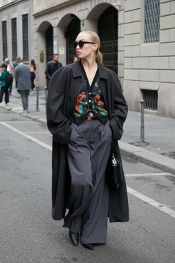 MILAN, ITALY - SEPTEMBER 25, 2022: Woman with black coat and gray trousers before Giorgio Armani fashion show, Milan Fashion Week street style