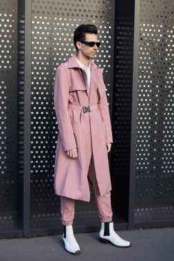 MILAN, ITALY - JANUARY 13, 2023: Man with pink trench coat and trousers and white boots before Gucci fashion show, Milan Fashion Week street style