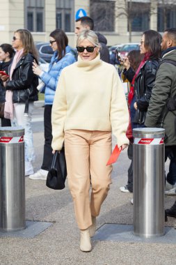 MILAN, ITALY - FEBRUARY 25, 2023: Woman with light yellow turtleneck and beige leather trousers before Ferragamo fashion show, Milan Fashion Week street style clipart