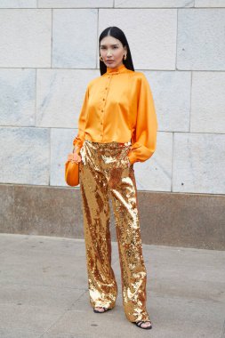 MİLAN, İtalya - 22 Şubat 2024: Altın pullu pantolon ve turuncu ipek gömlekli konuk Genny moda defilesinden önce, Milan Moda Haftası tarzı