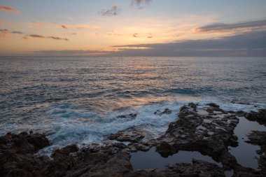 Beautiful sunset at the golden hour over the Atlantic Ocean near Palm-Mar resort with calm waters and frothy white waves and volcanic natural pools filling constantly, Tenerife, Canary Islands, Spain