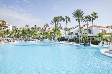 Hotel Parque Santiago III, Playa de las Americas, Tenerife, Kanarya Adaları, İspanya - 30 Aralık 2022: Yüksek palmiye ağaçlarıyla çevrili tropikal yüzme havuzu ve güneşli yataklarda dinlenen turistler tarafından keyif alındı