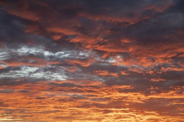 Fabulous sunset with clouds in intense radiant shades of crimson, purple and gold appearing ablaze and casting and ethereal glow over the entire sky, peaceful moment of the day before the nightfall