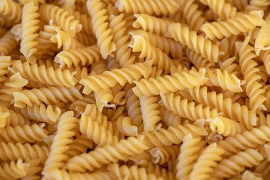 Altın fusilli kuru makarna, sarmal şekli ve sert dokusuyla, salatadan sağlıklı güveçlere kadar geniş bir yemek yelpazesi için mükemmel bir malzeme, dokulu yemek arkaplanı ve kırsal İtalyan cazibesi.