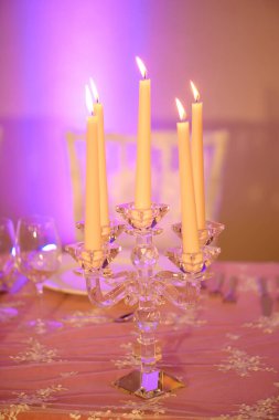 Güzel bir kristal şamdan ve yanan beş mum ile masa düzenleme, zarif ve dekoratif element özel durumlar, etkinlikler veya iç mekanlar için sıcak ve davetkar bir atmosfer oluşturmak için kullanılır.