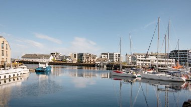 Alesund, Norveç - 1 Ağustos 2018: Zarif yatları ve sakin sulara demirlemiş geleneksel balıkçı tekneleriyle arka planda pitoresk kıyı kasabası bulunan büyüleyici körfezin manzarası