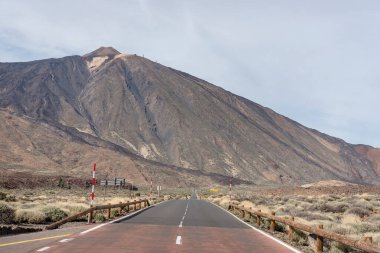 Boş yol, Las Canadas del Teide Ulusal Parkı, Tenerife, İspanya 'da bulunan Kanarya Adaları' nda Pico del Teide olarak bilinen görkemli Teide Dağı ile kurak volkanik manzarayla çevrilidir.