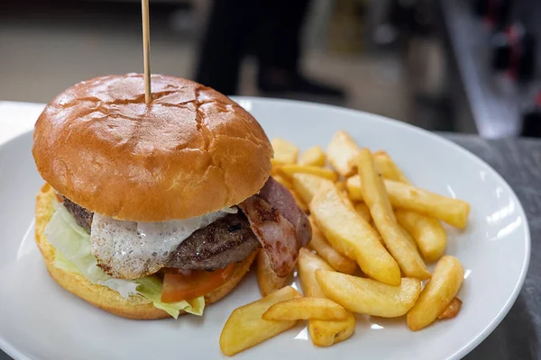 Large burger with egg and salad, and a big portion of fried chips aside set on a plate ready to be served, meal preferred for its taste, convenience and variety, consumed in different social occasions