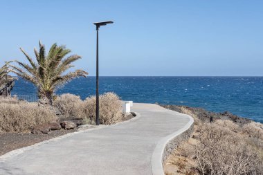 Volkanik engebeli kıyı şeridinde seyrek bitki örtüsü ve Tenerife, Kanarya Adaları, İspanya 'daki Amarilla Golf, Golf del Sur ve Los Abrigos arasında birkaç tatil beldesini birbirine bağlayan gezinti güvertesi.